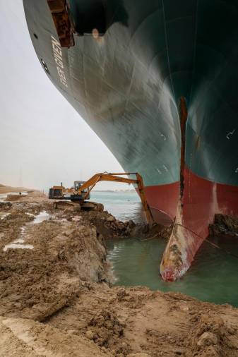 25 de marzo de 2021, Egipto, Suez: Una excavadora intenta liberar la parte delantera del “Ever Given”, un buque portacontenedores operado por Evergreen Marine Corporation. La estatal Autoridad del Canal de Suez (SCA) anunció el jueves que la navegación por el Canal de Suez ha sido suspendida temporalmente hasta la reflotamiento completo del superpetrolero panameño que encalló el martes en el extremo sur del Canal de Suez y bloqueó el tráfico en ambos. direcciones. El barco giró de costado en el Canal, mientras se dirigía de China a Rotterdam, debido a la visibilidad reducida que resultó de una tormenta de polvo que azotó el área, según SCA. (RECUPERAR) Foto: - / Autoridad del Canal de Suez / dpa
