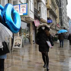 Imagen de archivo de unos transeúntes caminan protegidos por una calle de A Coruña, Galicia