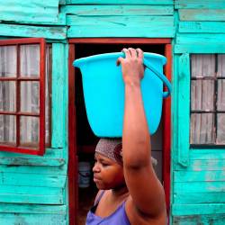Una estudiante sudafricana transporta agua en su cabeza desde una fuente pública a casa de sus padres. Esta fotografía fue tomada en Cape Town, Sudáfrica, en el año 2008. (Autor, Nic Bothm. Fuente, EFE)