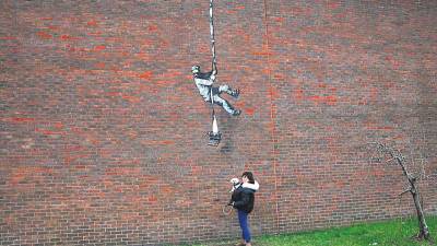 Una mujer con un perro se encuentra frente a la obra de arte de Banksy colocada en una pared lateral de una prisión en Reading, Gran Bretaña.