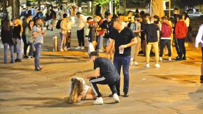 Joven tirada en el suelo y gente bebiendo en la calle en una noche de fiesta en Santiago