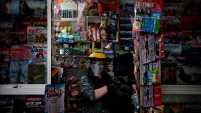 A CORUÑA, 22/05/2020.- Una mujer protegida con pantalla y mascarilla, atiende este viernes un kiosko de prensa en A Coruña. EFE/Cabalar