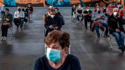 Varias personas esperan sentadas en caso de posibles efectos secundarios tras recibirla vacuna de AstraZeneca durante la campaña de vacunación masiva que se lleva a cabo estos días en el recinto ferial Expourense (Ourense). Foto: EFE/ Brais Lorenzo