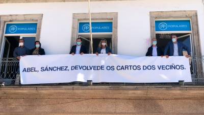 Diputados provinciales del área de Vigo desplegando el cartel en la sede local. Foto: M.Gimeno