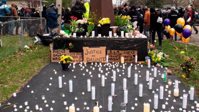 Velas y flores depositadas en el suelo frente a un cartel del movimiento Black Lives Matter durante una vigilia en recuerdo de Daunte Wright