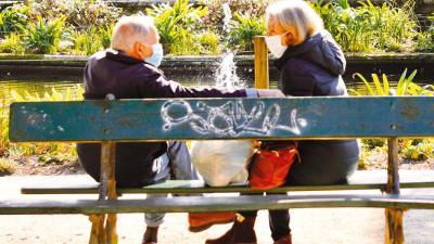 más personas mayores. Dos ancianos dialogan sentados en un banco de madera, en la Alameda de Santiago, en un día de sol. Foto: Fernando Blanco.