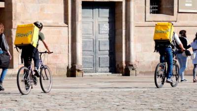 En bicicleta. Dos riders de la startup barcelonesa Glovo recorren sobre ruedas la reconocida plaza del Obradoiro para entregar a tiempo sus pedidos (Santiago). Foto: Antonio Hernández