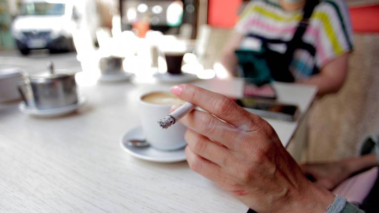 Una mujer fuma, este jueves, en la terraza de un bar de A Coruña, en una jornada en la que ha entrado en vigor la prohibición de fumar cuando, por tener personas próximas, no se pueda garantizar la preceptiva distancia de seguridad de dos metros. EFE/ CABALAR
