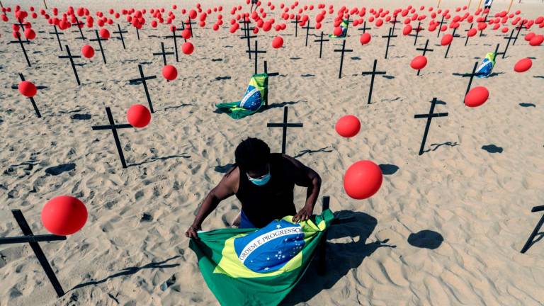 Copacabana. Activista instala una bandera de Brasil con los mil globos y cruces por las víctimas de la covid-19 en la mítica playa de Río de Janeiro (Brasil). Foto: Efe/Antonio Lacerda
