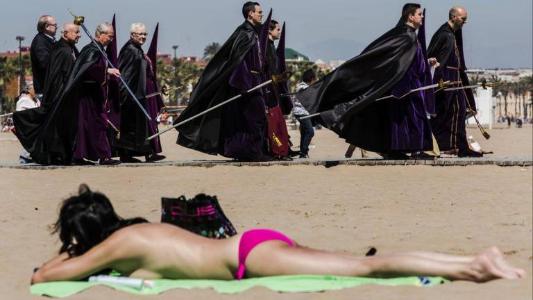 <b>Valencia</b>. Curiosa fotografía en la que bañistas y participantes en una procesión de Semana Santa se encuentran en la playa. (Fuente, rtve.es)