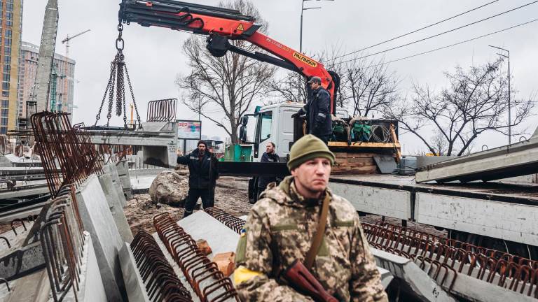 Varios operarios cargan losas de cemento frente a un miliciano ucraniano
