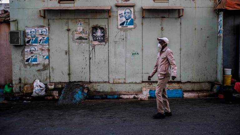 Un hombre camina junto a una tienda cerrada a causa de la pandemia de coronavirus en la capital de Senegal