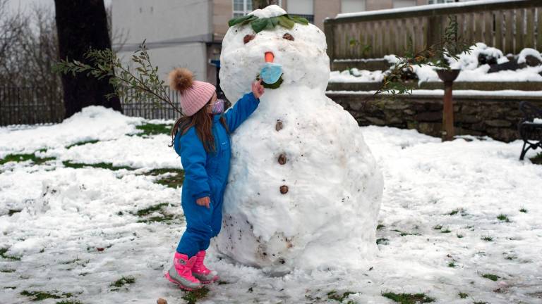 Una niña, protegida con la mascarilla, juega con su muñeco de nieve en Castro Caldelas, Ourense. (Autor, Brais Lorenzo. Fuente, EFE)