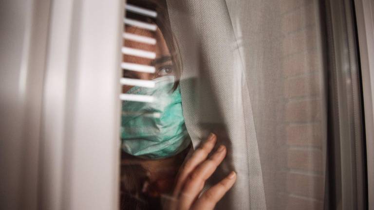 Foto de archivo de una mujer con mascarilla mirando por una ventana. MARIOGUTI/EUROPA PRESS