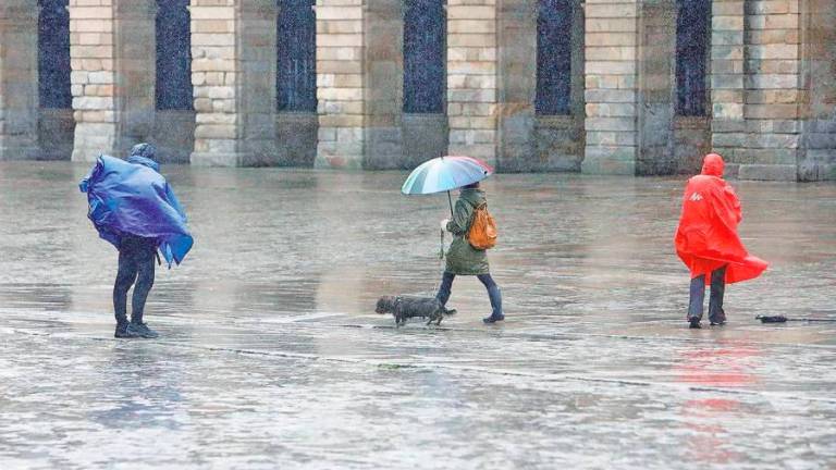 Una mujer bajo el paraguas paseando con su perro y dos peregrinos con chubasqueros, en la Praza do Obradoiro (archivo). Foto: Antonio Hernández