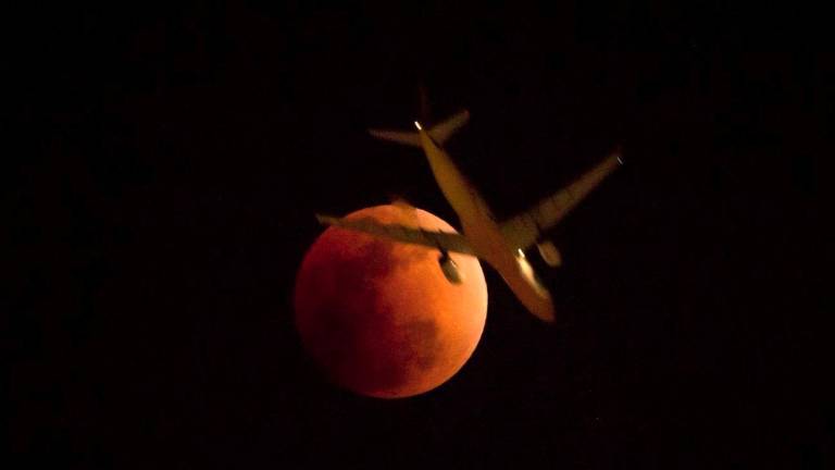 Un avión por el cielo negro de Hong Kong iluminado por la intensa luz rojiza de la Luna. (Fuente, eltribuno.com)