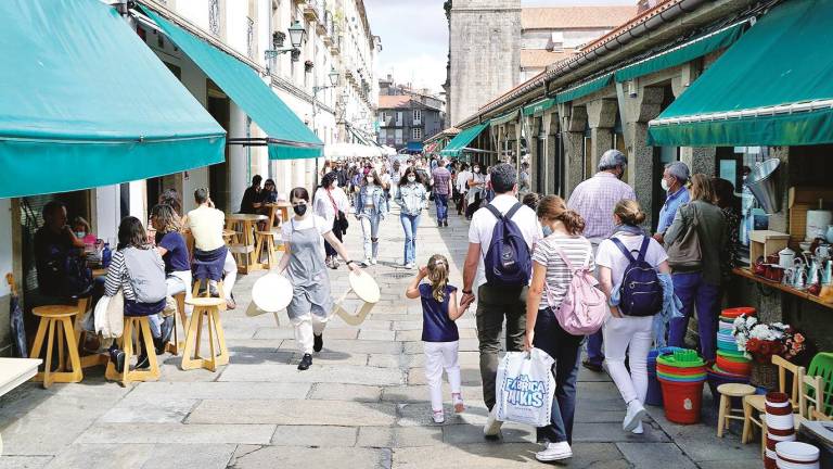 Galicia registró una pérdida de población en el último año que se sitúa en valores bajos en comparativa con el 1998. En la imagen, personas caminando y otras en terrazas de bares el pasado agosto, en Santiago de Compostela. Foto: Fernando Blanco.
