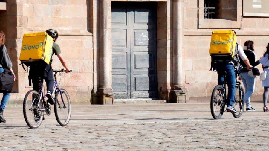 En bicicleta. Dos riders de la startup barcelonesa Glovo recorren sobre ruedas la reconocida plaza del Obradoiro para entregar a tiempo sus pedidos (Santiago). Foto: Antonio Hernández