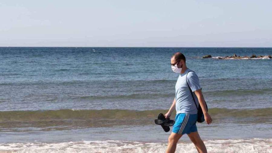En la foto de archivo, un hombre pasea por una playa con mascarilla. EFE