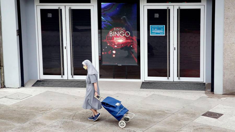 Una monja pasa con el carro de la compra delante del acceso a una de las salas de bingo de Santiago. Foto: Antonio Hernández