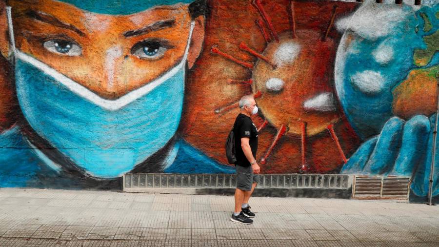 en la calle. Un hombre camina junto a un mural en homenaje a los sanitarios que han estado en primera línea en la batalla contra el coronavirus en una calle de Melide, en la provincia de A Coruña. Foto: Eliseo Trigo/Efe 