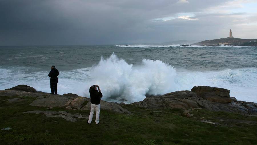 Dos personas hacen fotos de olas rompiendo contra la costa en la ciudad de A Coruña, el pasado sábado. EFE/Cabalar