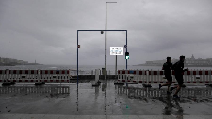 A CORUÑA, 12/08/2020.-Dos hombres corren este miércoles por el paseo marítimo de A Coruña, frente al semáforo que regula la entrada peatonal a la playa de Riazor, en una jornada en la que continúa activa la alerta naranja por lluvias. EFE/ CABALAR