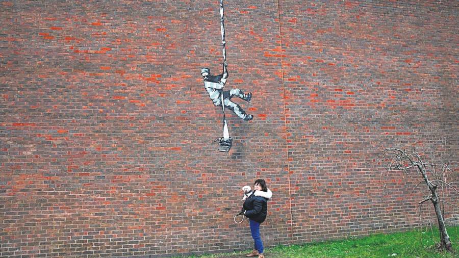 Una mujer con un perro se encuentra frente a la obra de arte de Banksy colocada en una pared lateral de una prisión en Reading, Gran Bretaña.
