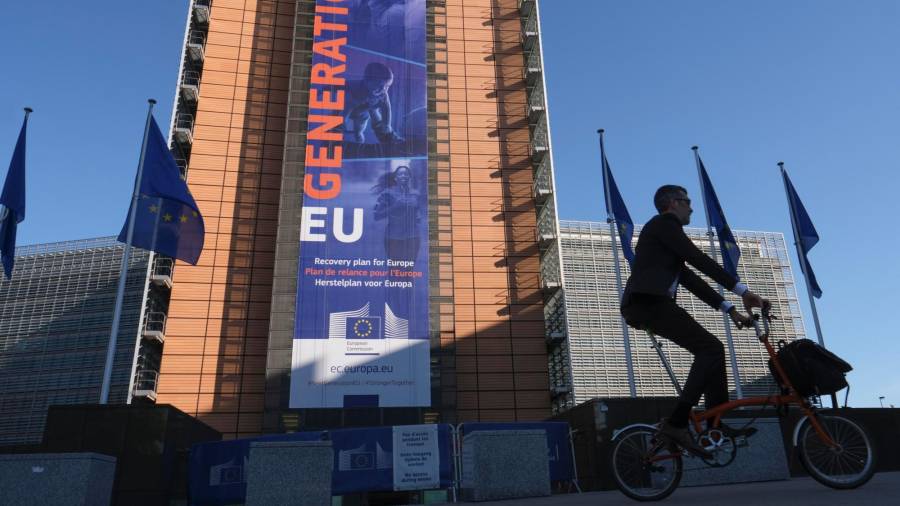 Un hombre pasa con su bicicleta ante la sede de la Comisión Europea en Bruselas, sobre cuya fachada cuelga un enorme cartel en el que se hace referencia al Plan de Recuperación de la Unión Europea. Foto: Olivier Hoslet/Efe