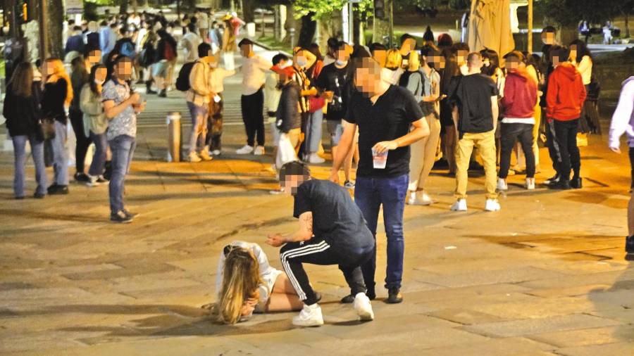 Joven tirada en el suelo y gente bebiendo en la calle en una noche de fiesta en Santiago