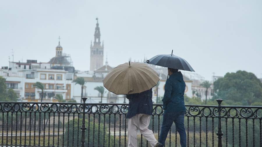 Una pareja cruzando el Puente de Isabel II en un día lluvioso del puente de Todos los Santos el 30 de octubre de 2021 en Sevilla (Andalucía, España) / Joaquin Corchero / Europa Press 30/10/2021