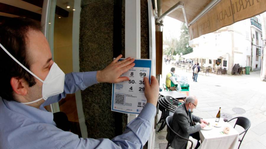 Un hostelero coloca el cartel con los aforos y el código QR en su establecimiento. Foto: F. Blanco
