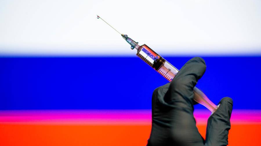 Una jeringuilla con una dosis de vacuna contra el coronavirus y, al fondo, la bandera rusa Foto: E.P.