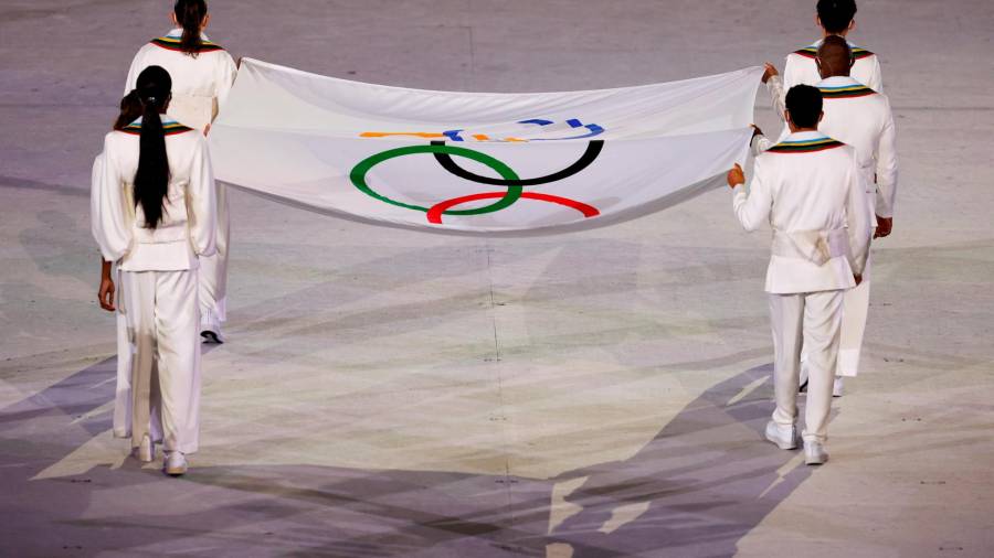 Operarios portan la Bandera Olímpica durante la ceremonia inaugural de los Juegos Olímpicos de Tokio 2020. Foto: Enric Fontcuberta