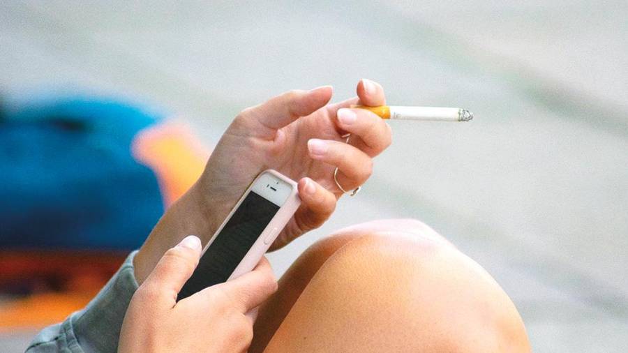 Una mujer fuma un cigarrillo mientras consulta su teléfono móvil. Foto: Angy A.E.