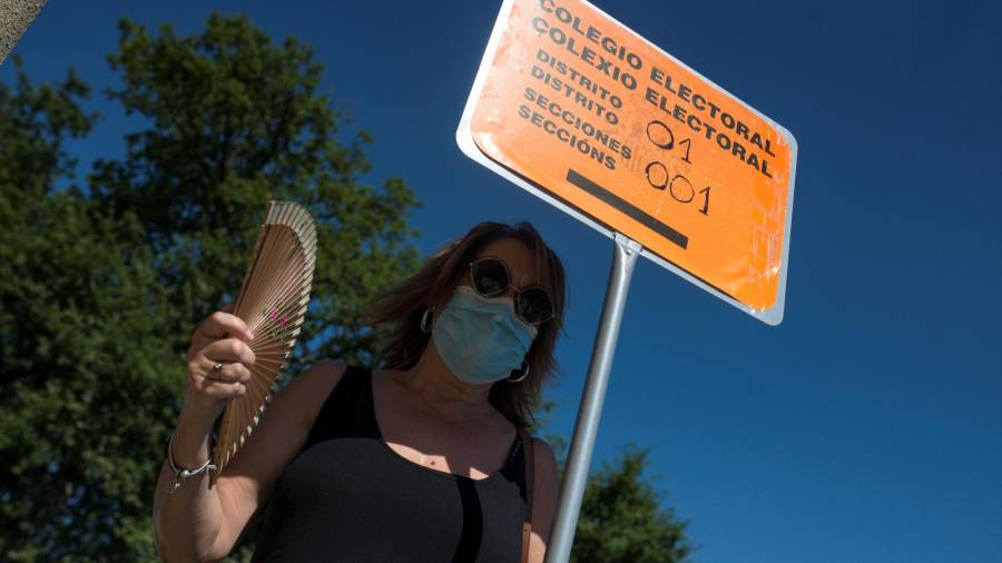 En la foto, del pasado martes, una mujer combate el calor junto a una señal de colegio electoral en Pereiro de Aguiar (Ourense). EFE/Brais Lorenzo