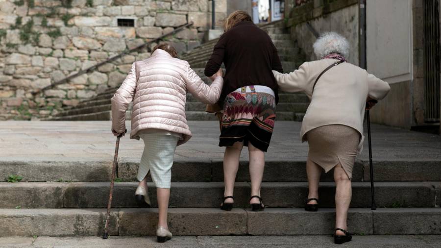 Unha cuidadora, centro da imaxe, axuda a dúas mulleres maiores na súa vida cotiá. Foto: XG