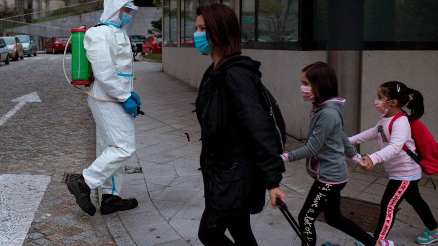 Un operario realiza labores de desinfección en una calle de Ourense mientras una mujer acompaña a dos niñas al colegio. Foto: Brais Lorenzo/Efe