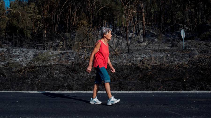 TOÉN (OURENSE), 08/08/2020.- Una mujer camina junto a la superficie calcinada en el incendio forestal que permanece activo en el municipio orensano de Toén. EFE/Brais Lorenzo