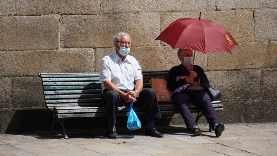 Dos personas, con mascarilla, descansan en un banco ayer en Santiago. FERNANDO BLANCO