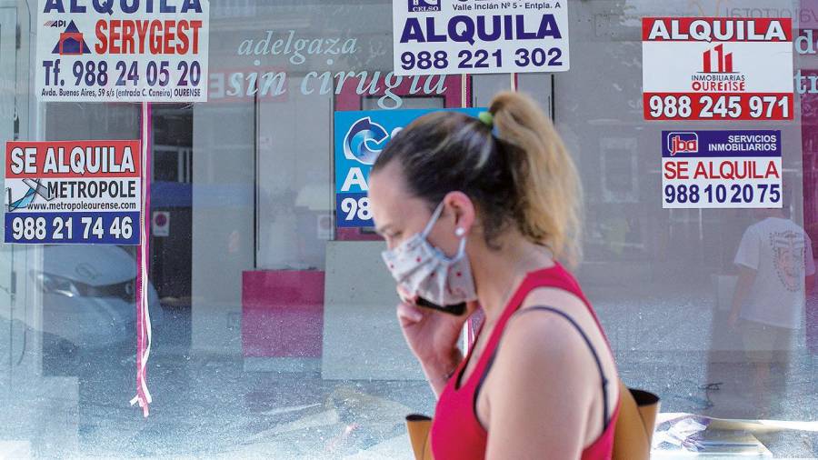 Imagen de una mujer pasando delante de un establecimiento cerrado, en la ciudad de Ourense, con varios carteles que anuncian su alquiler. Foto: Brais Lorenzo/Efe 