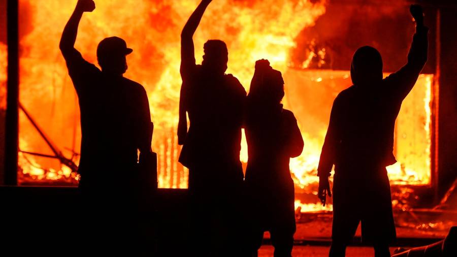 Manifestantes alzan el puño junto a una tienda en llamas en Mineápolis. Craig Lassig 