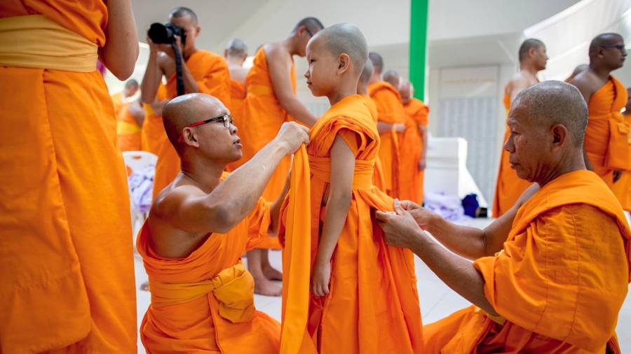 Monjes budistas ayudan a un joven novicio a ponerse la túnica para su ordenación en el templo tailandés de Wat Pra Dhammakaya. (Autor, Diego Azubel Fuente EFE)