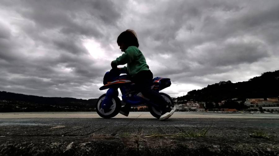 Un niño jugando en una moto de juguete en la jornada de ayer en el paseo marítimo de Cabanas, A Coruña, sobre un cielo gris amenazante de lluvia Foto: EFE/Cabalar