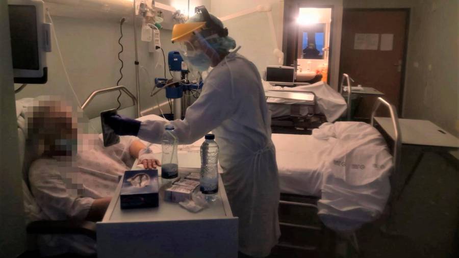 Un voluntario facilita una videollamada de un paciente con un familiar en el hospital Clínico