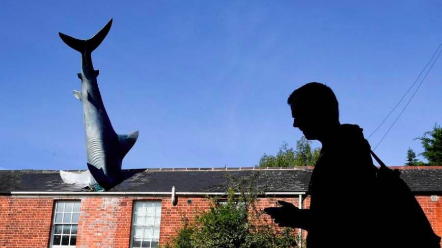 Un hombre pasa junto a una escultura de fibra de vidrio de 1986, comúnmente llamada “The Headington Shark”, que está incrustada en el techo de una casa en Oxford, Inglaterra. Autor, Toby Melville. (Fuente, www.businessinsider.es)