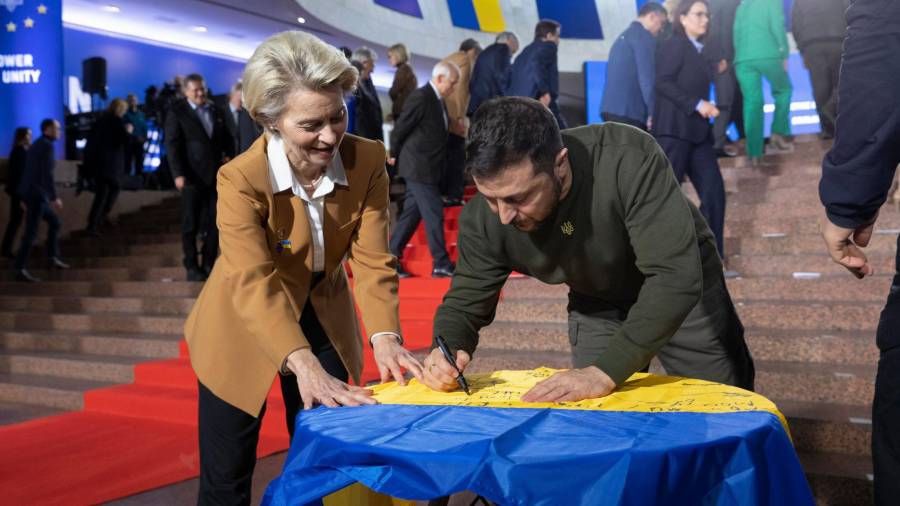 Volodímir Zelenski firma una bandera de su país ante Ursula von der Leyen. Foto: Efe