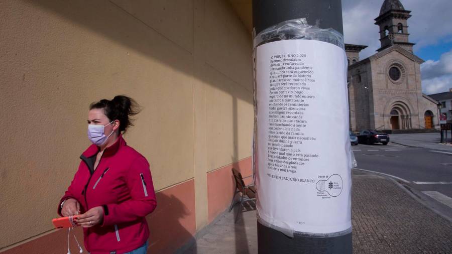 Una mujer camina frente a una farola donde hay pegado un papel con un poema titulado ‘El virus chino 2020’, en el municipio gallego de Guitiriz, en Lugo. FOTO: Carlos Castro