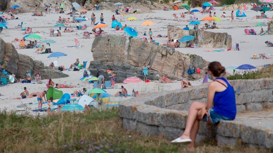Una persona sentada frente a la playa en A Mariña en julio de 2020. Carlos Castro
